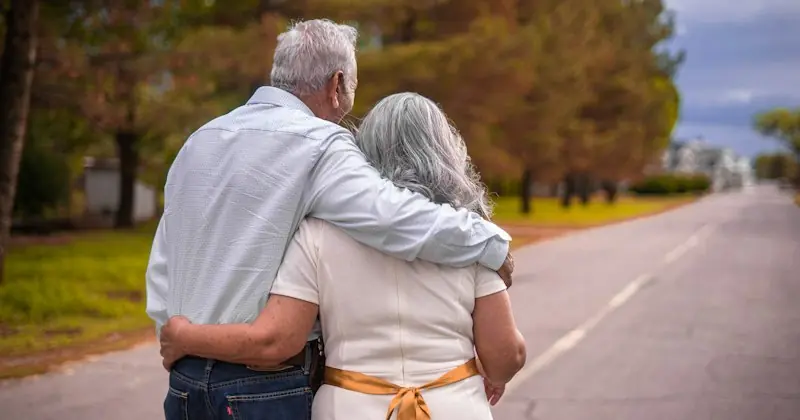 Ein älteres Paar geht Arm in Arm eine Landstraße entlang